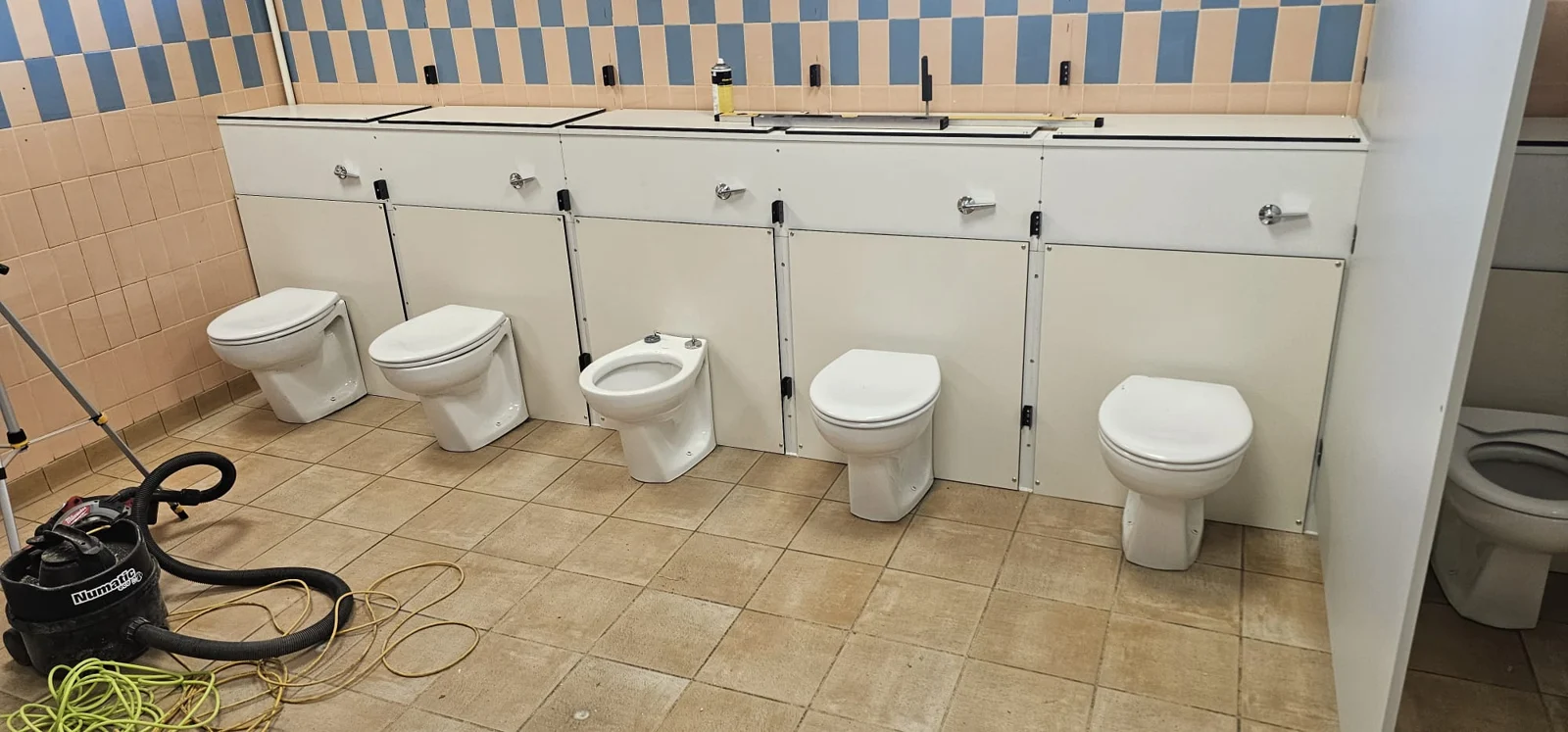 Toilets and service boxing along the tiled wall