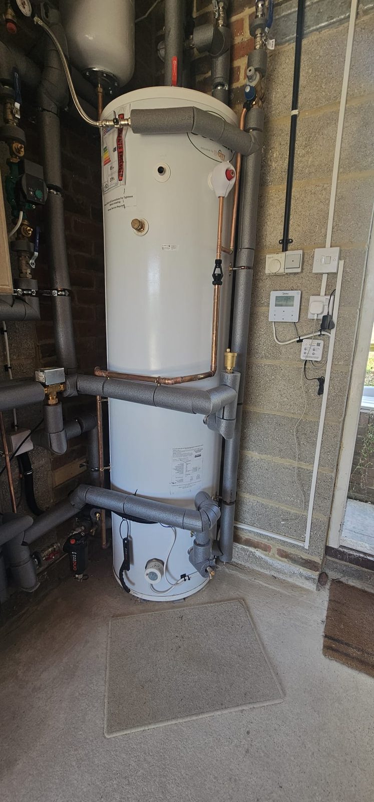 Hot water cylinder alongside wall-mounted system controls and switches