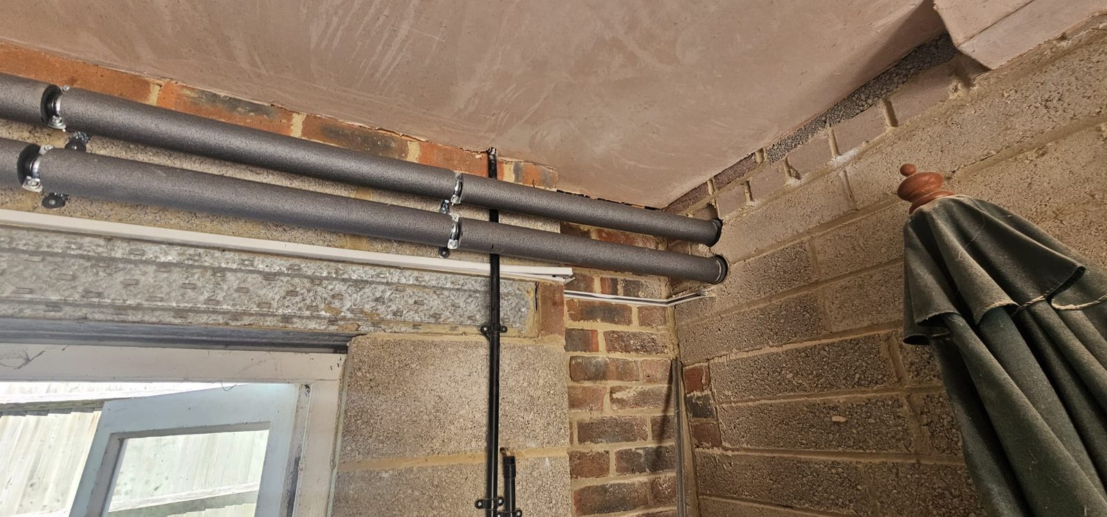 Insulated pipe runs clipped neatly along a brick and block wall below the ceiling